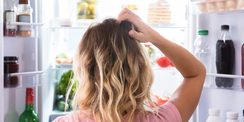 Confused Woman Looking In Open Refrigerator